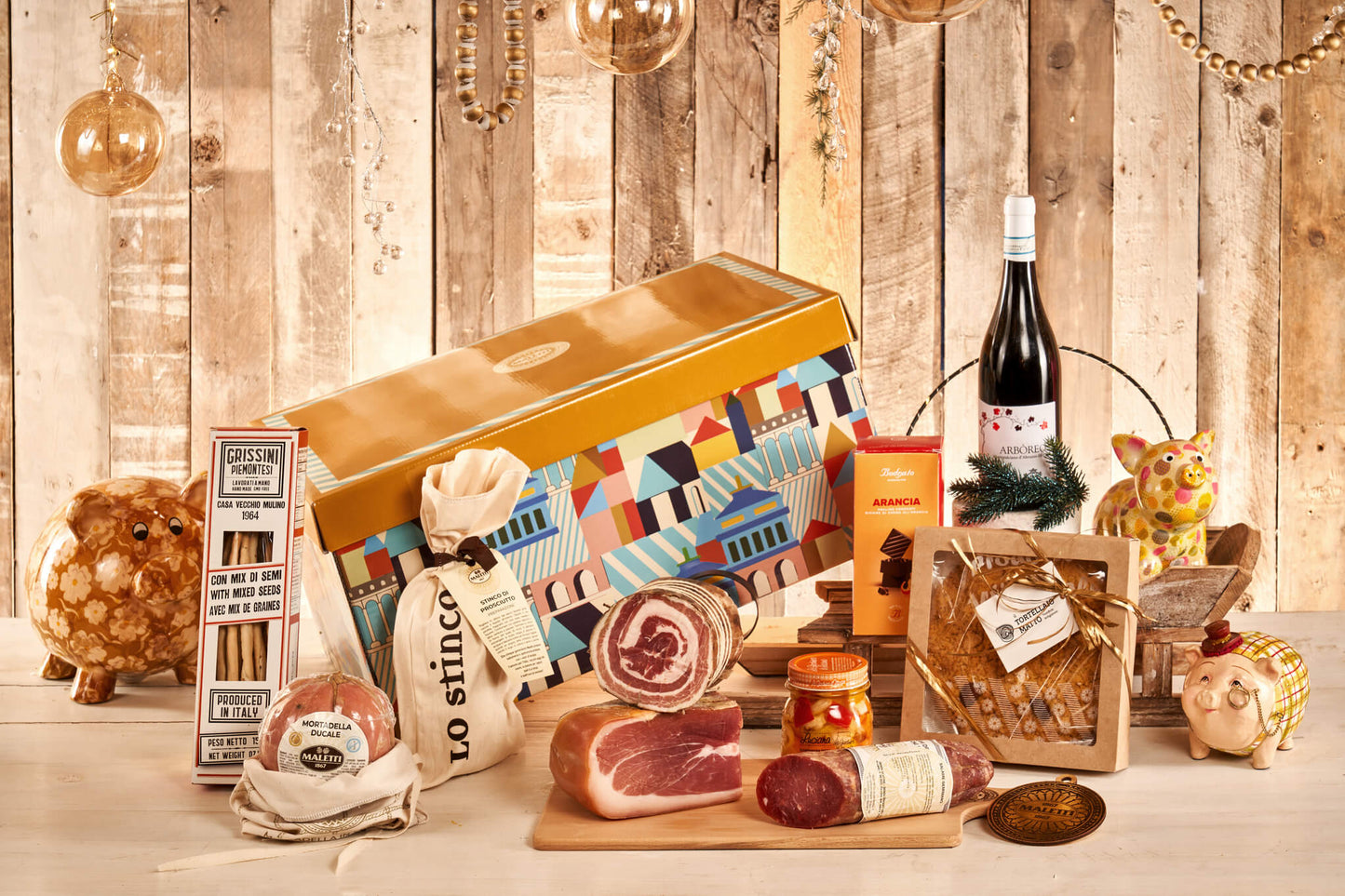 Confezione regalo di vizioDiVino chiamata "I tre norcini". All'interno contiene: torta sbrisolona 300 g; stinco in sacchetto Maletti 650 g; grissini piemontesi ai semi 150 g; praline fondenti all’arancia 120 g; trancio prosciutto scelto 1,3 kg; giardiniera "di Luciana" 250 g; trancio pancetta al pepe nero Maletti 450 g; mortadella vescica naturale con sacchetto tela 900 g; salame Geminiano a metà sv 500 g; bottiglia di Montepulciano d’Abruzzo D.O.C. 75 cl.